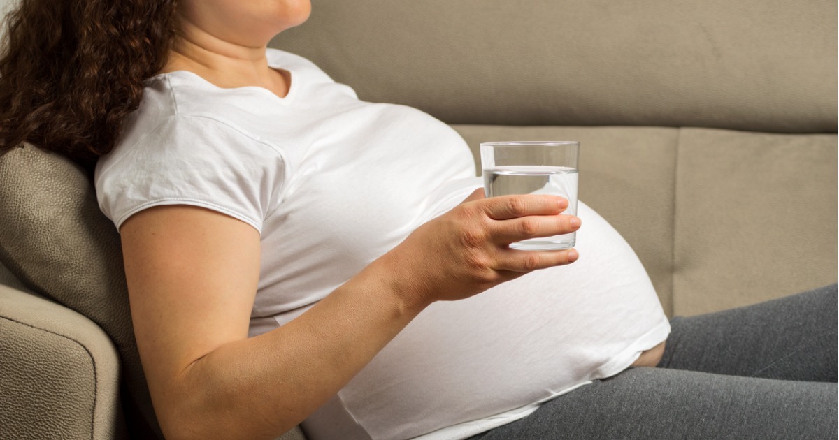 A pregnant woman is sitting with a glass of water.